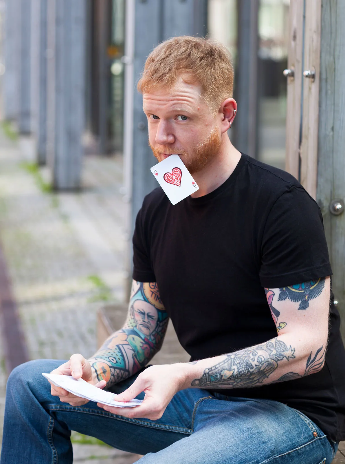 Matthew Austin sitting outdoors, holding a deck with a playing card between the teeth