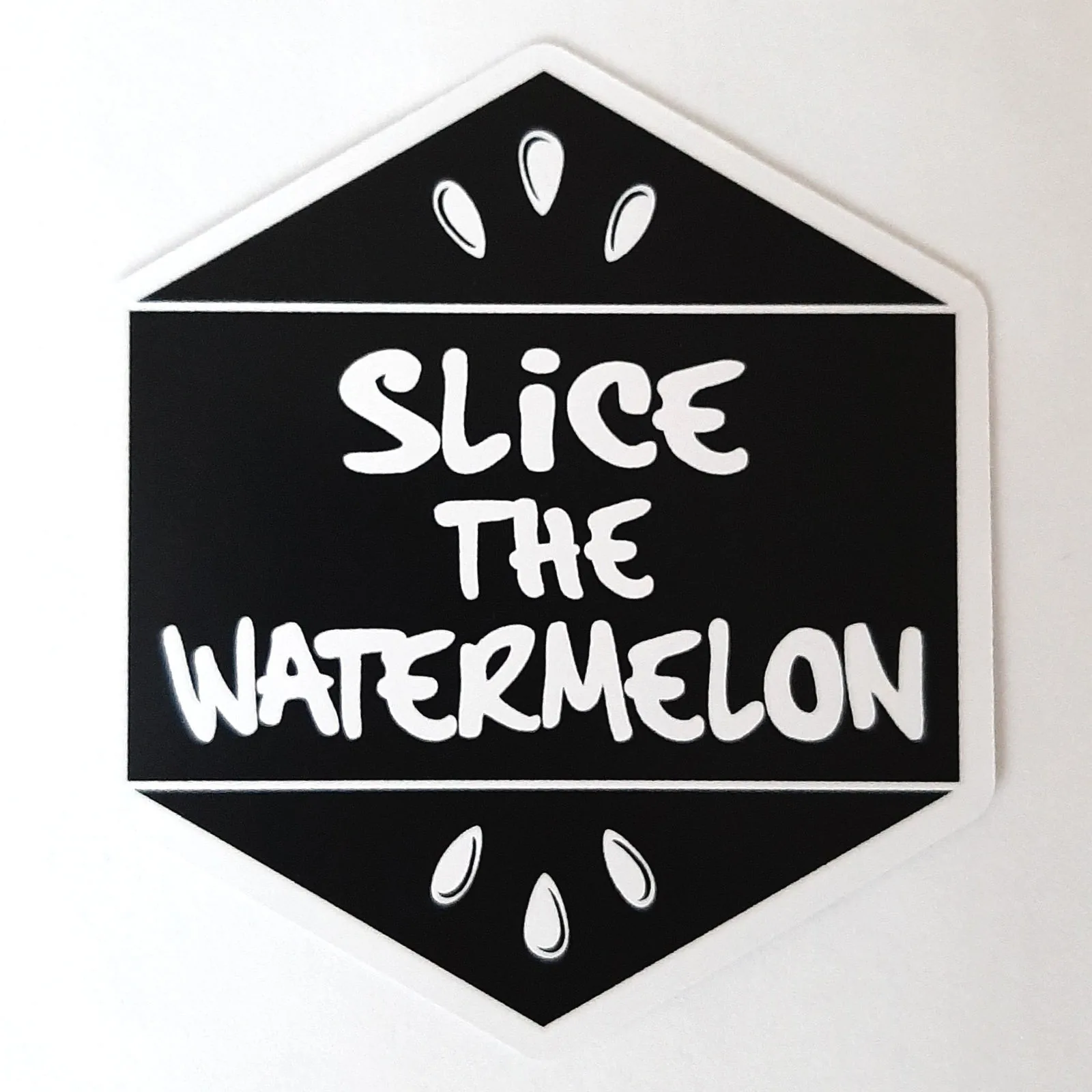 Black hexagon tile back with the Slice the Watermelon logo